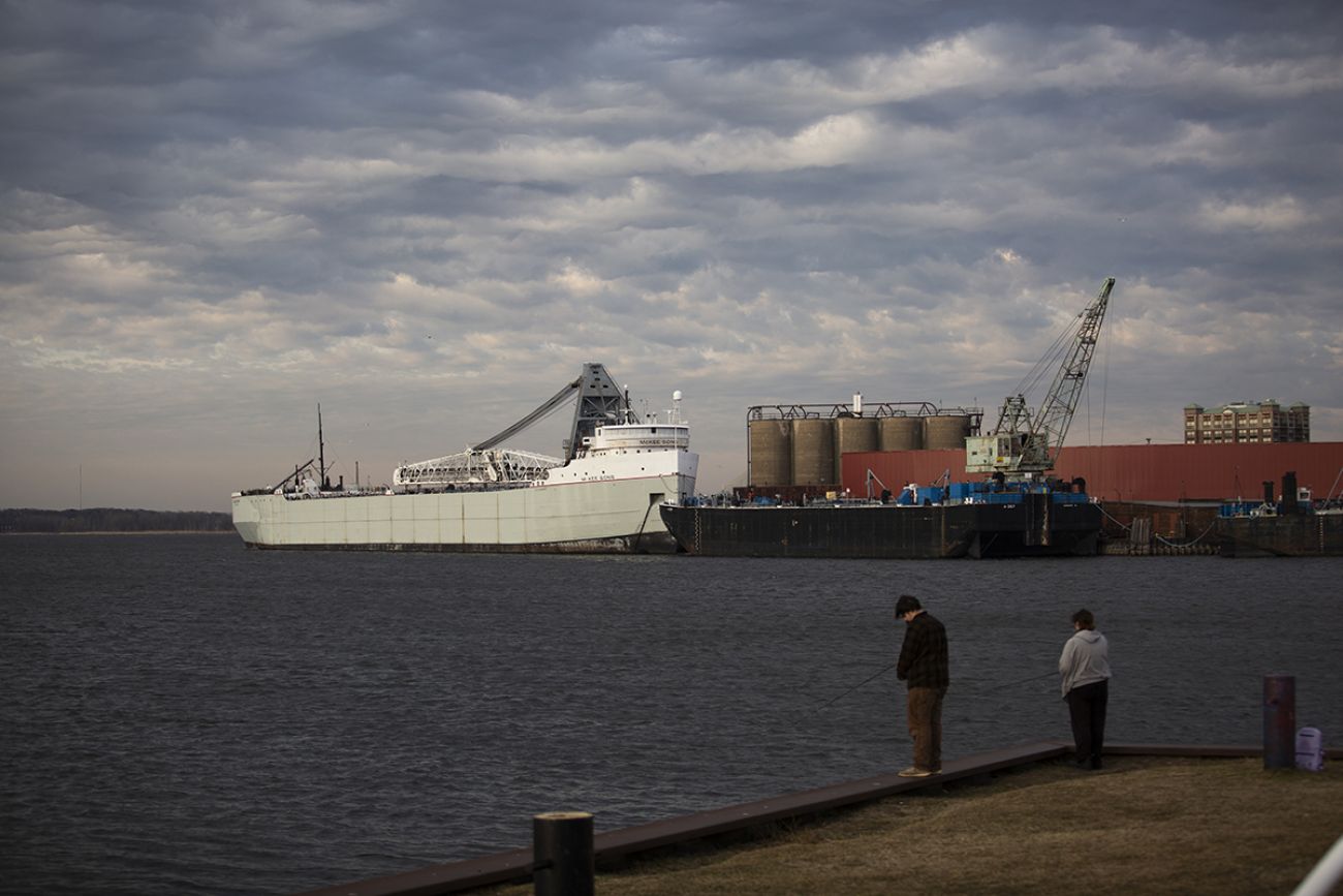 Two people are the foreground. Ships are in the background.