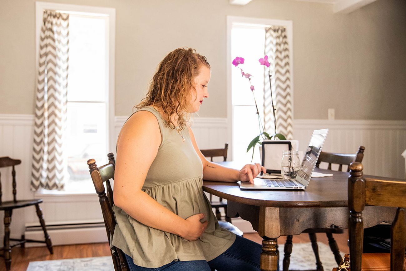 Abby Gilmore at a desk holding her stomach 