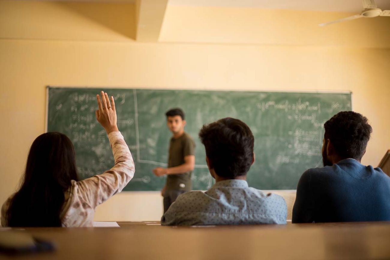 Group of student sitting at their desks and one student raised her hands to ask doubt to teacher.