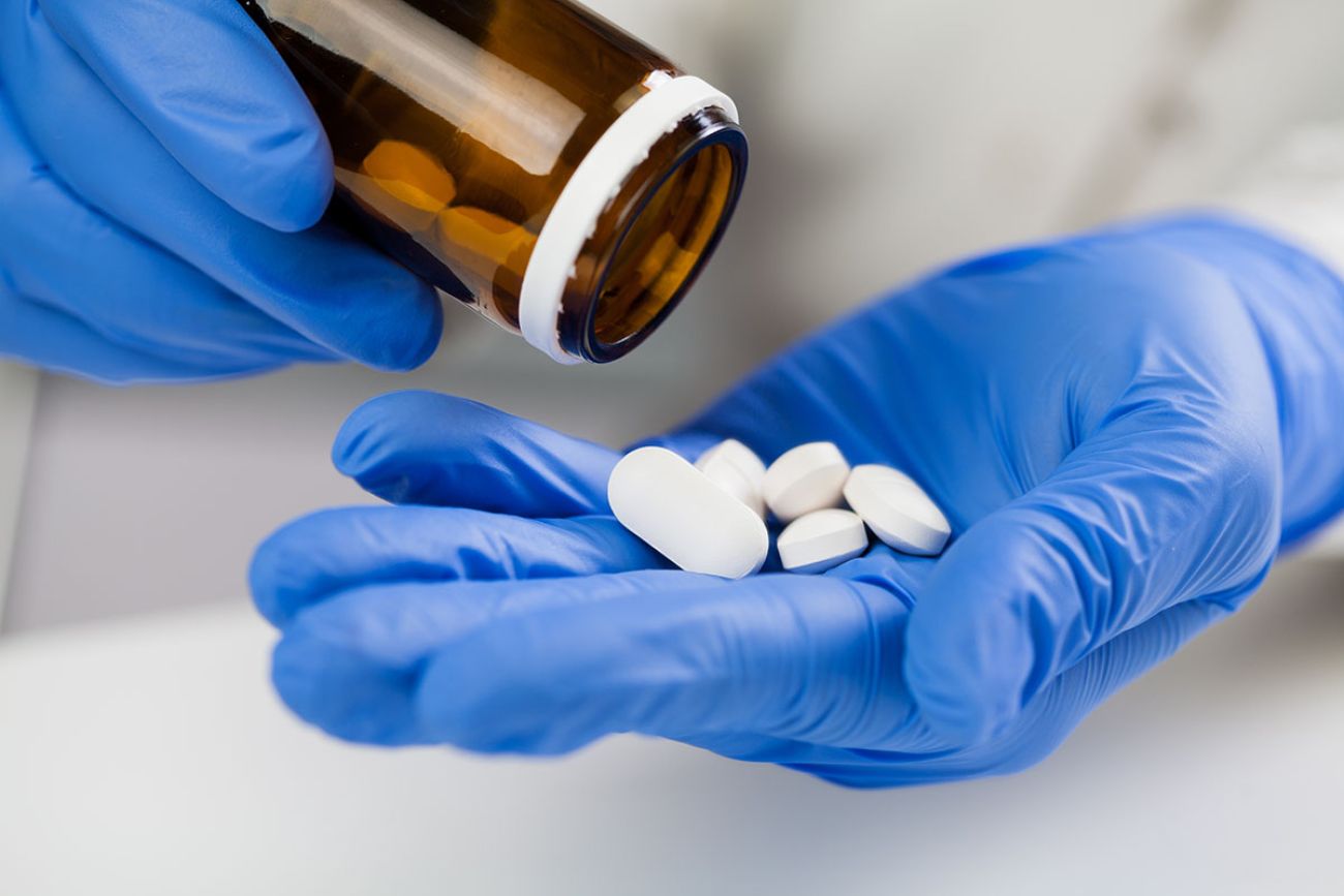 medical practitioner wearing blue surgical latex gloves holding medicine bottle,taking out several white pills