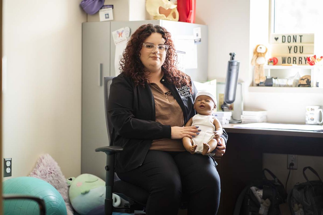 Fatima Barba sitting in a chair, holding a doll. She's in an office