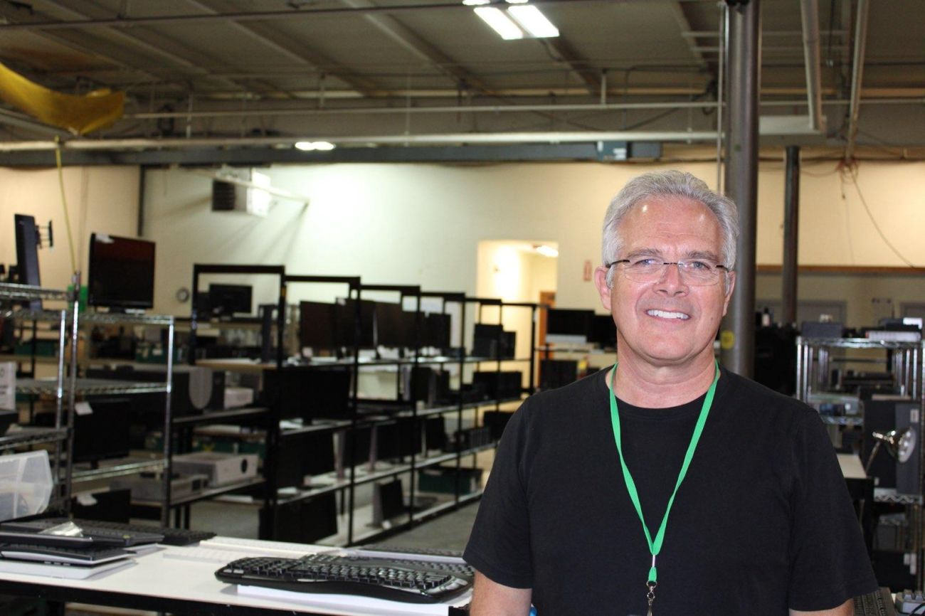 Scott VanderKooy standing in a room. In the background, there are shelfs of laptops