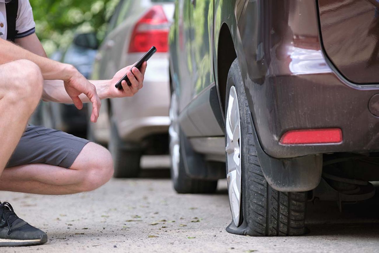 Driver calling road service for assistance having vehicle trouble with punctured flat tire on car parked on roadside