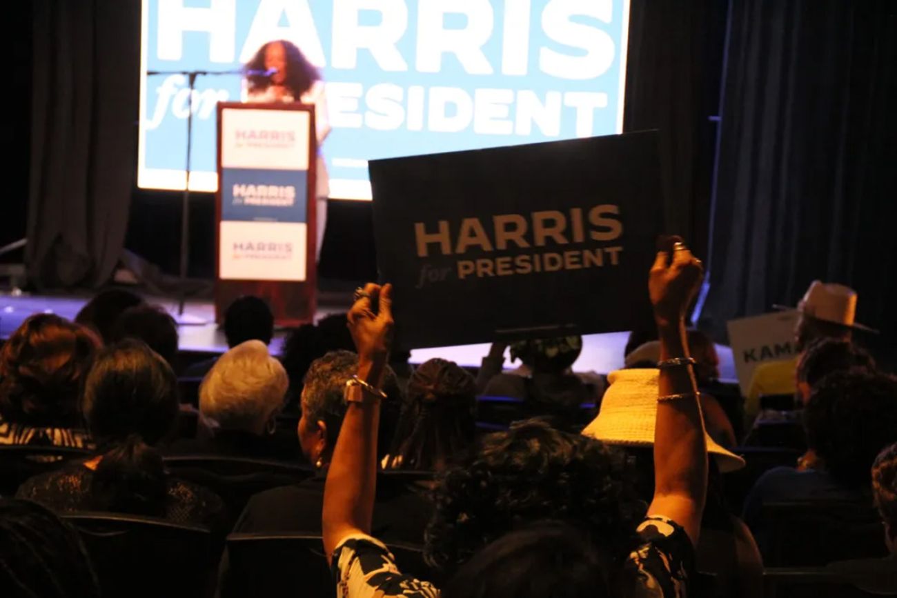 Someone holding up a "Harris for President" sign in an auditorium