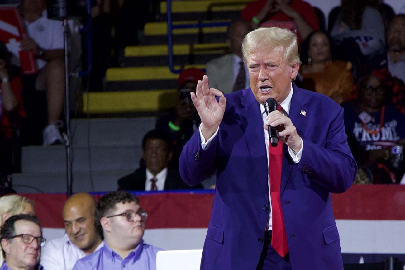 Donald Trump, wearing a blue suit, talking into a microphone