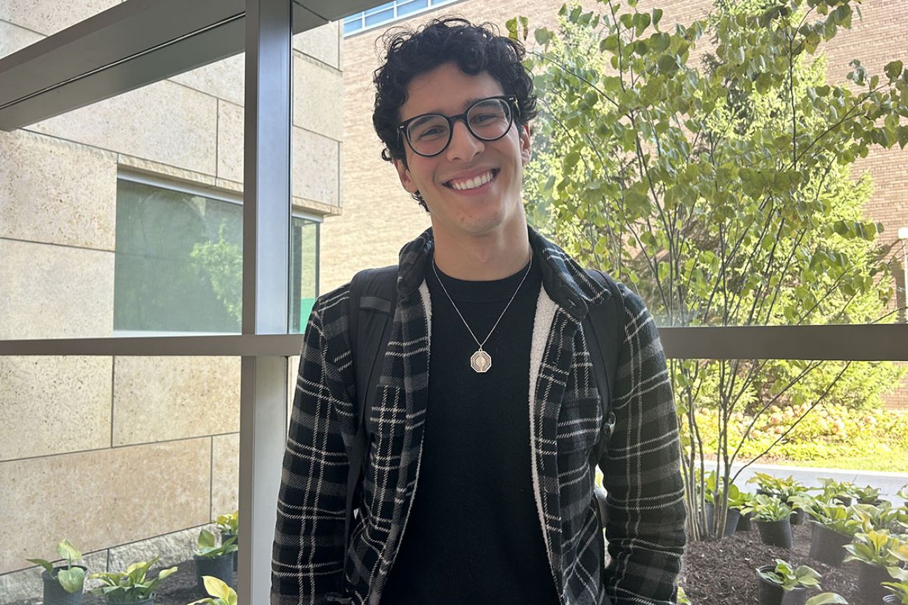 Mustafa Alithawi, wear a black t-shirt and dark-colored sweat shirt, poses for a picture in front of windows