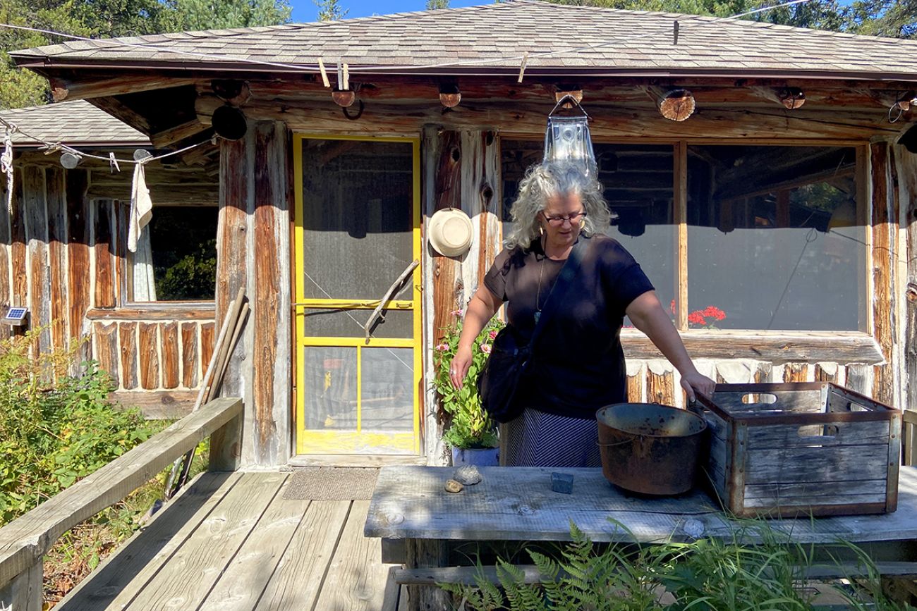 Kathleen Heideman stands in front of her cabin on a sunny day