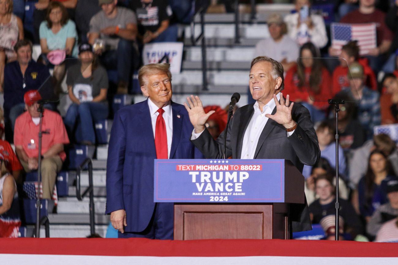 Mike Rogers is on stage at a Donald Trump rally. The former president is standing next to him