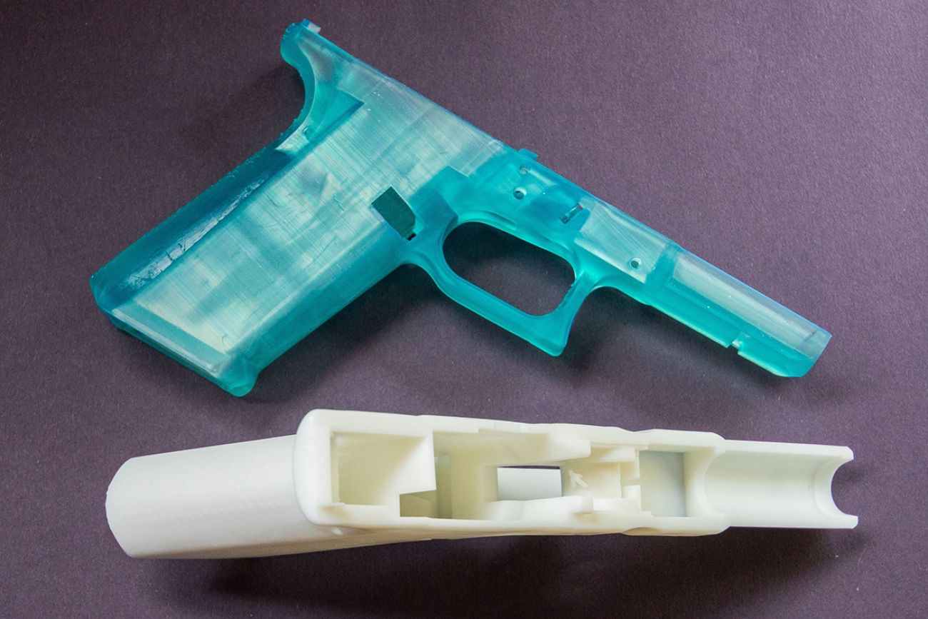 A closeup of 3D printed turquoise and white "Ghost Gun" on a dark background.