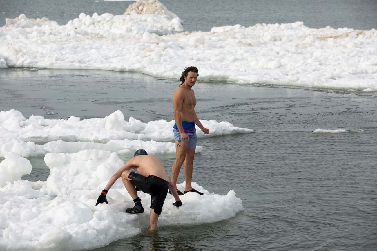 Two men with swim suits. There''s snow on the ground. One of the men is climbing out of water.