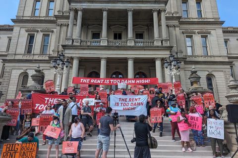 people with signs that says "rent is too damn high" in front of the capitol