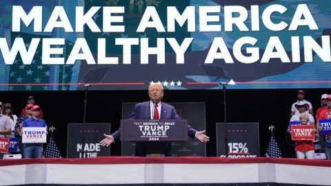 Former President Donald Trump at a rally, a sign in the back says "Make America Wealthy Again"