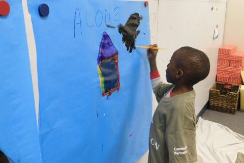 A boy paints on paper hanged on the wall