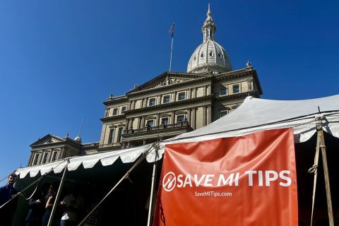 A sign says "Save MI Tips" in front of Michigan Capitol building.