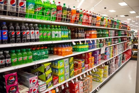 A view of the soda aisle of a grocery store, featuring several brands and colors of carbonated beverages.