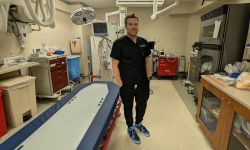 Dr. Bryce Bredell, wearing black scrubs, stands in a room with medical equipment 