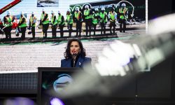 Gov. Gretchen Whitmer speaking on stage. Behind her is a photo of a groundbreaking. 