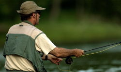 A man fishing. He is wearing green and white clothes.