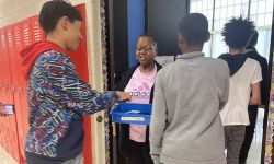 Kids put the cellphones in a container held by a teacher. 